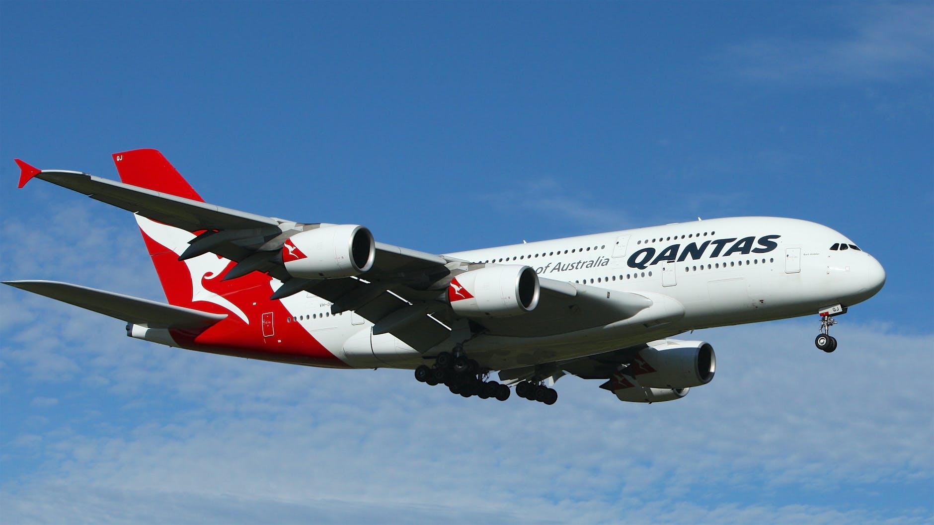 white and red qantas airplane fly high under blue and white clouds